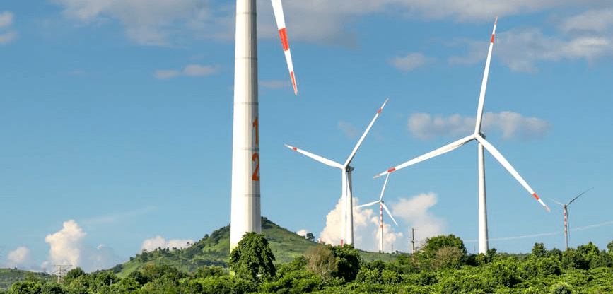A line of wind turbines on a green hillside under a clear sky.